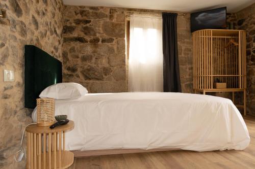 a bedroom with a white bed and a stone wall at Ecolagar O Barqueiro in Pantón