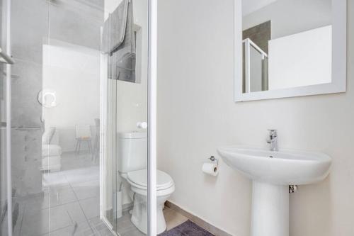 a white bathroom with a toilet and a sink at Grandeur by Mall of Africa in Midrand