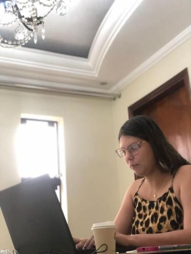 a woman sitting at a table using a laptop computer at Quarto com varanda tipo Airbn b Vista Panorâmica Livre da Cidade in Americana