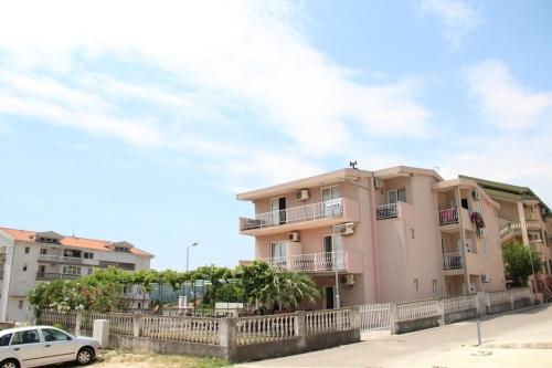 um edifício de apartamentos cor-de-rosa com um carro branco estacionado em frente em Apartments Petricevic em Sutomore