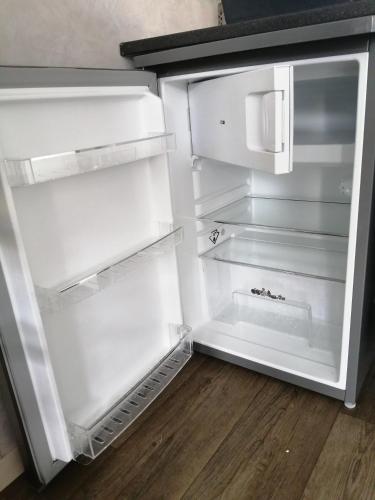 - un réfrigérateur vide avec une porte ouverte sur du parquet dans l'établissement Appartement meublé 1 étoile - Tourisme tout confort - Cures et Courts séjours - Les Mascareignes, à Châtel-Guyon