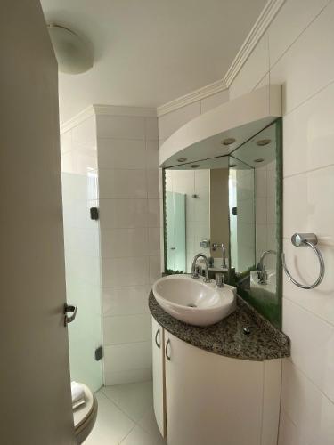 La salle de bains est pourvue d'un lavabo et d'un miroir. dans l'établissement Apartamento com sacada e churrasqueira, à Balneário Camboriú