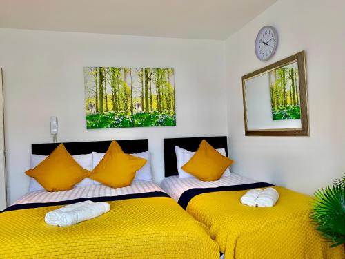 two beds in a room with yellow pillows and a clock at London Studio Apartments Close to Station NP6 in London