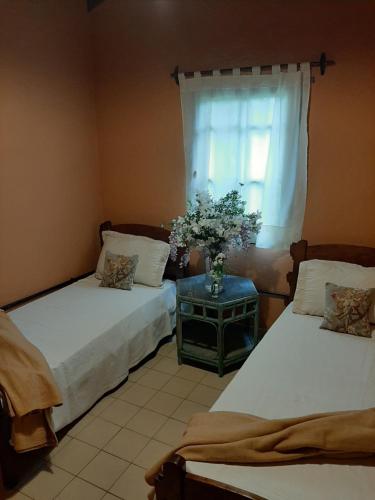 1 dormitorio con 2 camas y un jarrón de flores sobre una mesa en Delta Rose Farm en Tigre