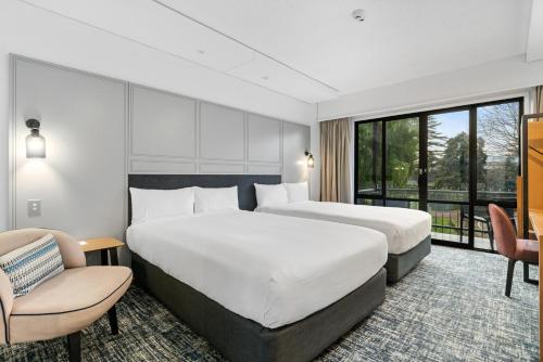a hotel room with two beds and a chair at Chateau On The Park - Christchurch, A Doubletree By Hilton in Christchurch