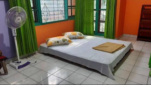 a bedroom with a bed with green curtains and a fan at Guest House Dorm Floressa in Maumere