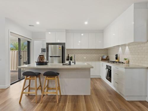 a kitchen with white cabinets and two bar stools at Rosella Retreat in Yarrawonga