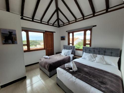 a bedroom with two beds and two windows at HOTEL ALTIPLANO VILLA DE LEYVA in Villa de Leyva