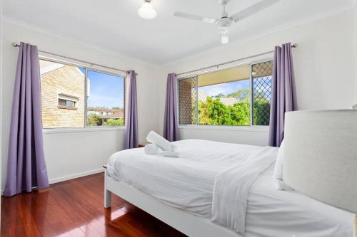 a white bedroom with a bed and two windows at Winston Waves in Bongaree