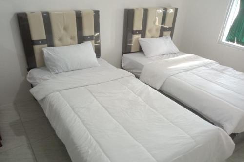 Cette chambre comprend 2 lits avec des draps et des oreillers blancs. dans l'établissement OYO 93100 Harapan Homestay Syariah, à Parit