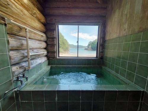 a bathroom with a tub with a window at Pension Shishikui in Shishikui