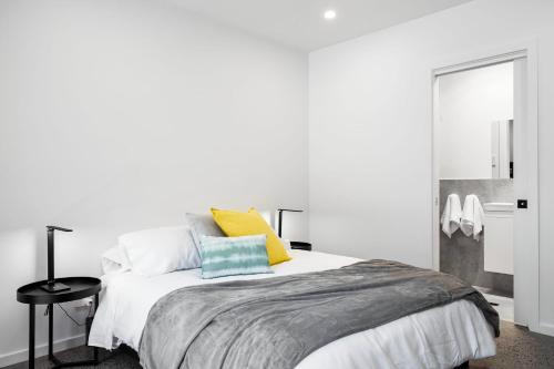 een witte slaapkamer met een bed met gele en blauwe kussens bij Lemon & Salt Studio Glenelg South in Glenelg