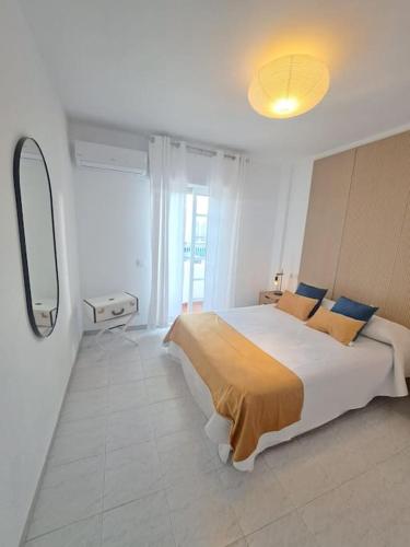 a white bedroom with a large bed and a mirror at Dúplex 8, en primera línea de playa in Sanlúcar de Barrameda
