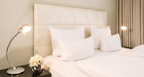 Una cama blanca con almohadas blancas y una lámpara en una mesa. en Best Western Victor's Residenz-Hotel Rodenhof en Saarbrücken