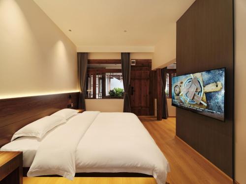 een slaapkamer met een groot wit bed en een flatscreen-tv bij Saturday Inn in Lijiang