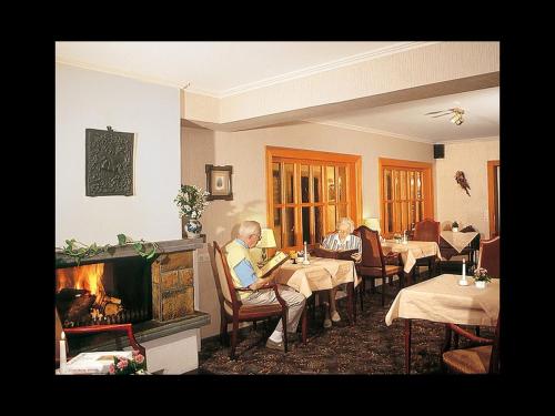 two people sitting at tables in a restaurant with a fireplace at Gasthof Heimes in Schmallenberg