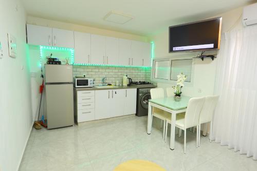 a kitchen with white cabinets and a table and a refrigerator at דירה יפה סגנון מודרני מרחק של 5 דקות נסיעה מהים in Ashkelon
