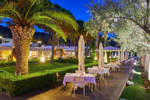 a row of tables with white umbrellas and palm trees at Ortunc Hotel - Cunda Island (Adult Only) in Ayvalık