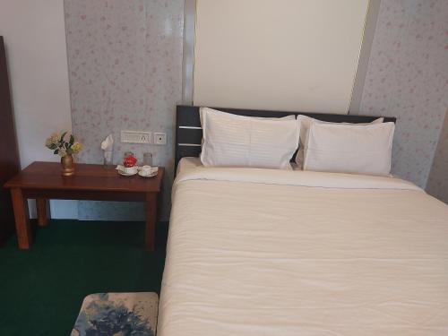 a bed with white sheets and a nightstand next to a table at Norbulingka Retreat in Gyalzing