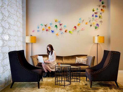 a woman sitting on a couch with a laptop at Mövenpick Hotel Auckland in Auckland