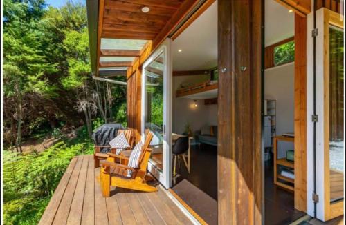 a house with a wooden deck with chairs on it at Fantail’s Nest in the forest in Takaka