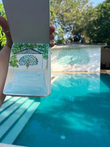 a person holding up a book next to a swimming pool at Sapphire Garden Hotel in Habarana