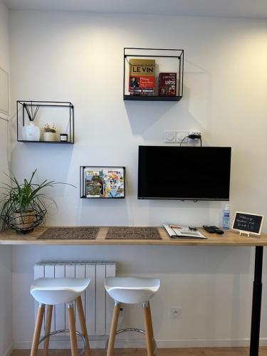 escritorio con 2 taburetes y TV en la pared en La Cabotte - Confort & Charme au Centre Historique - Balcon sur cour en Dijon