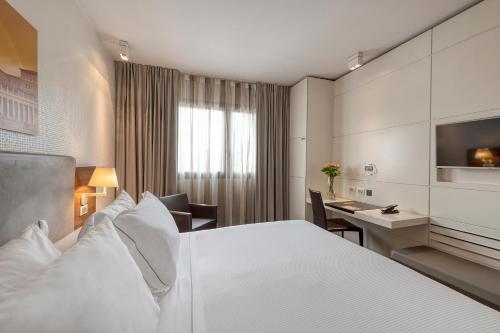 a hotel room with a large white bed and a desk at H10 Roma Città in Rome