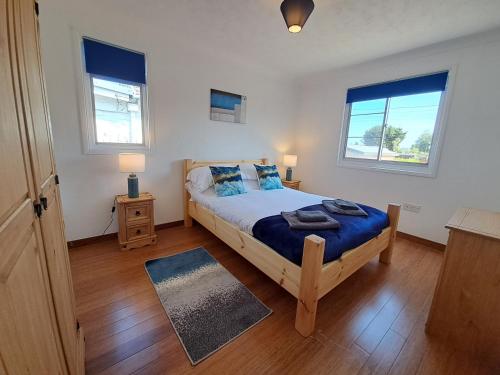 a bedroom with a bed with blue sheets and two windows at River View - Norfolk Broads in Brundall