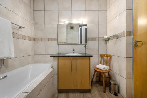 ein Badezimmer mit einer Badewanne, einem Waschbecken und einem Stuhl in der Unterkunft Hibernian Towers 309 Strand - Luxury Self Catering in Kapstadt