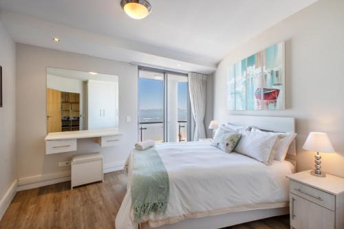 a white bedroom with a large bed and a desk at Hibernian Towers 309 Strand - Luxury Self Catering in Cape Town