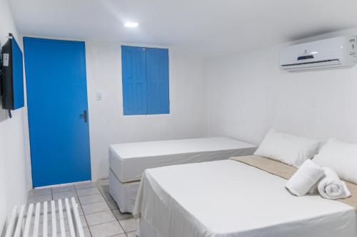 um quarto branco com 2 camas e uma porta azul em Pousada La Bella Luna em Porto de Galinhas