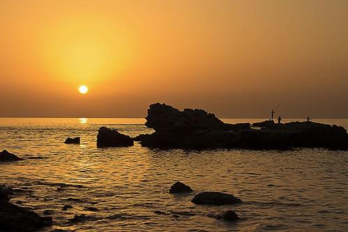 a person fishing on the rocks in the ocean at sunset at Suite paradise - E013 garden apartment in Caesarea