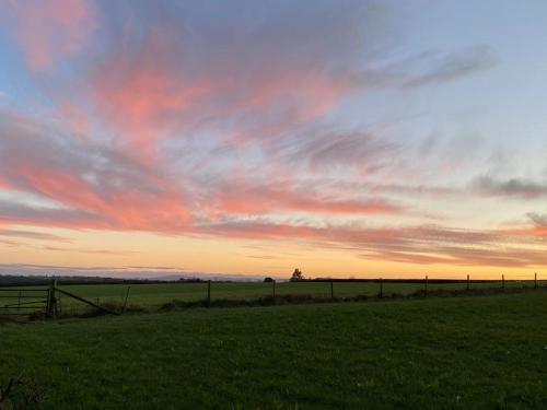 a field with a fence and a sunset in the sky at Bedport Loft in Burrington