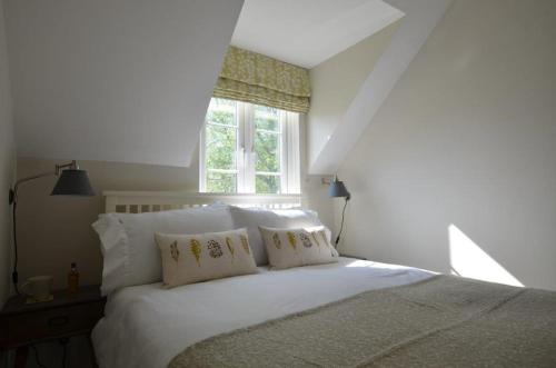 a bedroom with a white bed with pillows and a window at Elouera, 21 Isis Lake in South Cerney