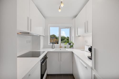 cocina blanca con fregadero y ventana en Tranquil 1 Bed Flat in East London, en Londres
