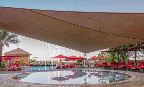 une grande piscine avec des chaises rouges et des parasols rouges dans l'établissement Amwaj Rotana, Jumeirah Beach - Dubai, à Dubaï