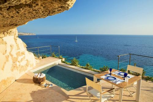 a pool with a table and chairs and the ocean at Cap Rocat, a Small Luxury Hotel of the World in Cala Blava