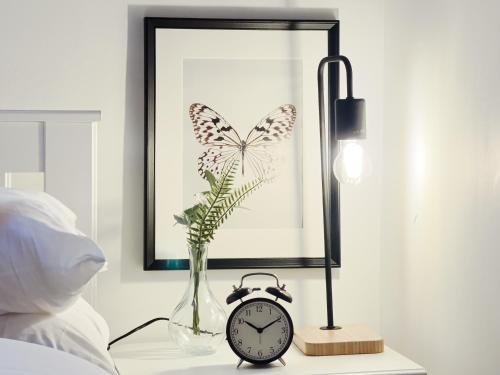 a table with a clock and a butterfly picture and a lamp at Peaceful Retreat: Work & Leisure in London