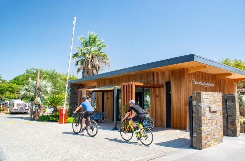 two people riding bikes in front of a building at Au Paradis des Campeurs in Les Issambres