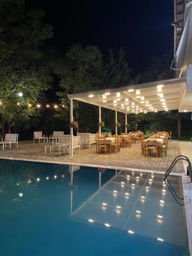 a patio with tables and chairs next to a swimming pool at night at Hotel Aroma in Përmet