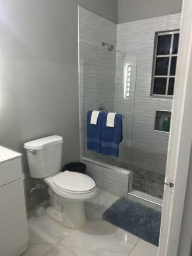 a bathroom with a toilet and a shower with blue towels at Oak Villa MontegoBay2 Queen Room in Montego Bay