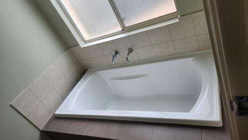 Beeliar Shared Home Stay في Coogee: حوض استحمام أبيض في حمام مع نافذة