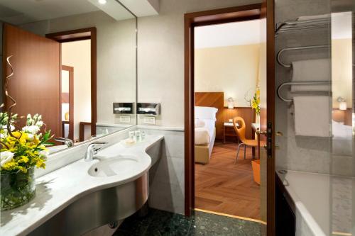 a hotel bathroom with a sink and a bedroom at UNAHOTELS Mediterraneo Milano in Milan