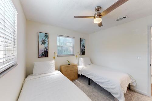 2 Betten in einem Zimmer mit weißen Wänden und einem Deckenventilator in der Unterkunft Lounging Palms Estate in Fort Myers