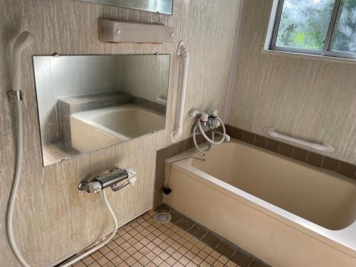 ein Bad mit einer Badewanne und einem Spiegel in der Unterkunft 北アルプス麓のゲストハウス林屋 203 in Ō-shinden