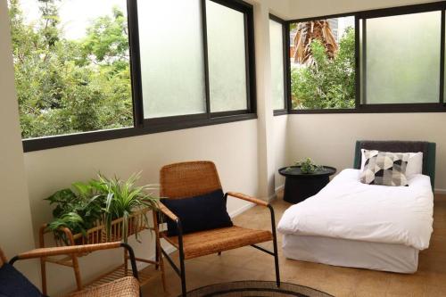 a room with a bed and a chair and windows at Bright and Cozy Bauhaus Gem in Ra‘ananna
