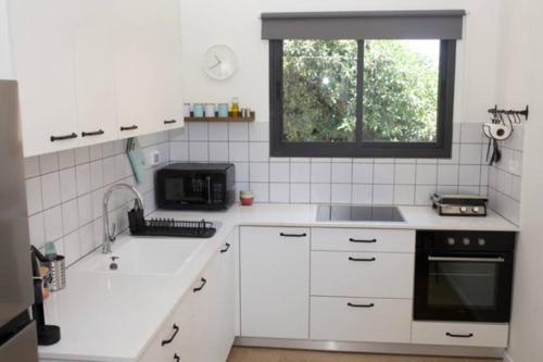 a white kitchen with a sink and a microwave at Bright and Cozy Bauhaus Gem in Ra‘ananna