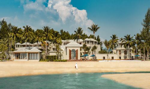 a person standing in the water in front of a house at Devasom Khao Lak Beach Resort & Villas in Khao Lak