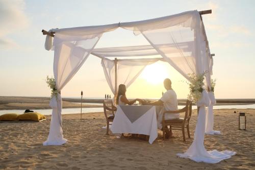 a couple sitting at a table under a tent on the beach at Devasom Khao Lak Beach Resort & Villas in Khao Lak